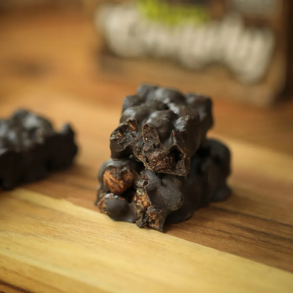 Barra de cereais crocantes biO2 cortada ao meio, vegana e sem glúten, sabor caramelo e cacau com cobertura de chocolate meio amargo, em cima de uma tábua de madeira