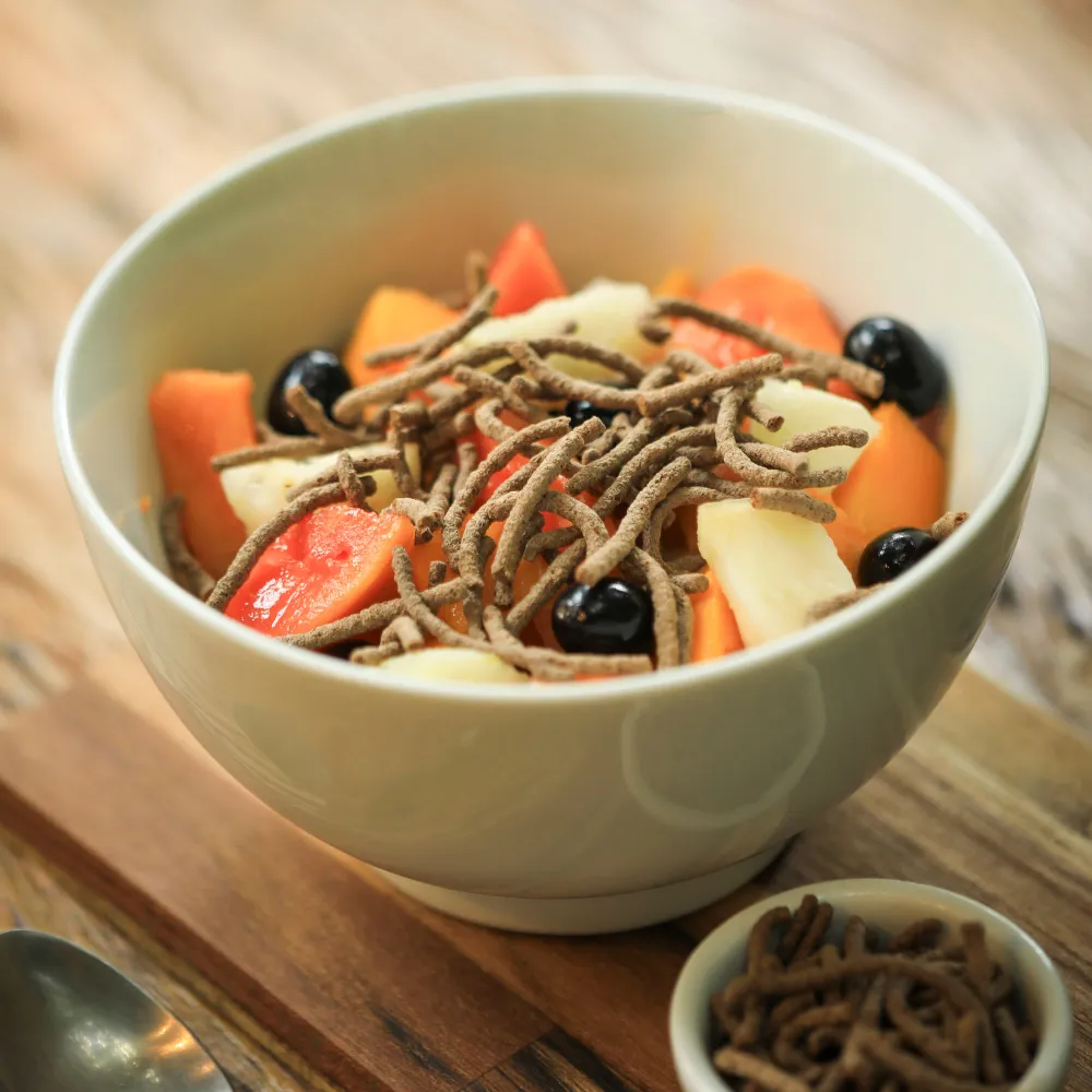 Tigela com um mix de frutas e em cima o cereal matinal proteico e fibras biO2, vegano e sem glúten.