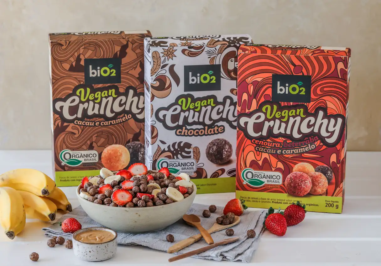 Cereais matinais biO2 3 sabores em uma mesa com um bowl de com frutas