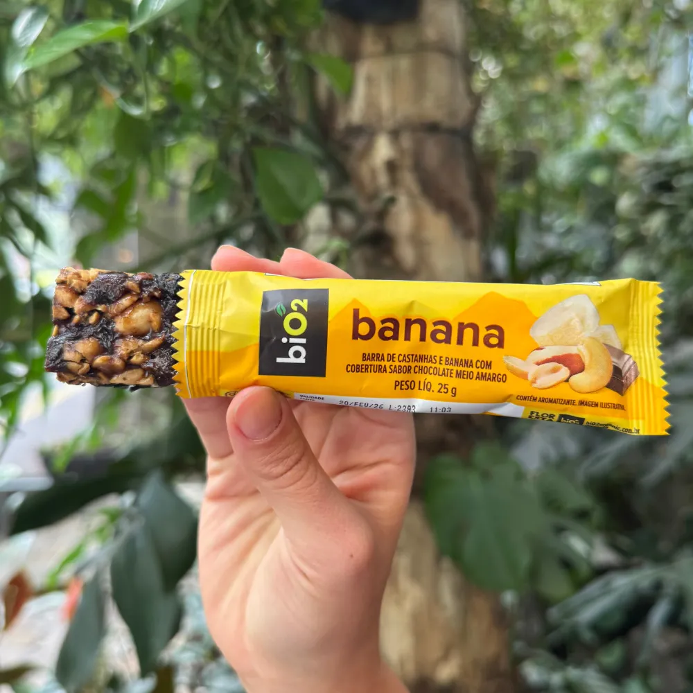 Parte da barra de Castanhas e Frutas biO2, vegana e sem glúetn, sabor Banana com chocolate, para fora da embalagem de 25 gramas, exibindo a textura da barra.