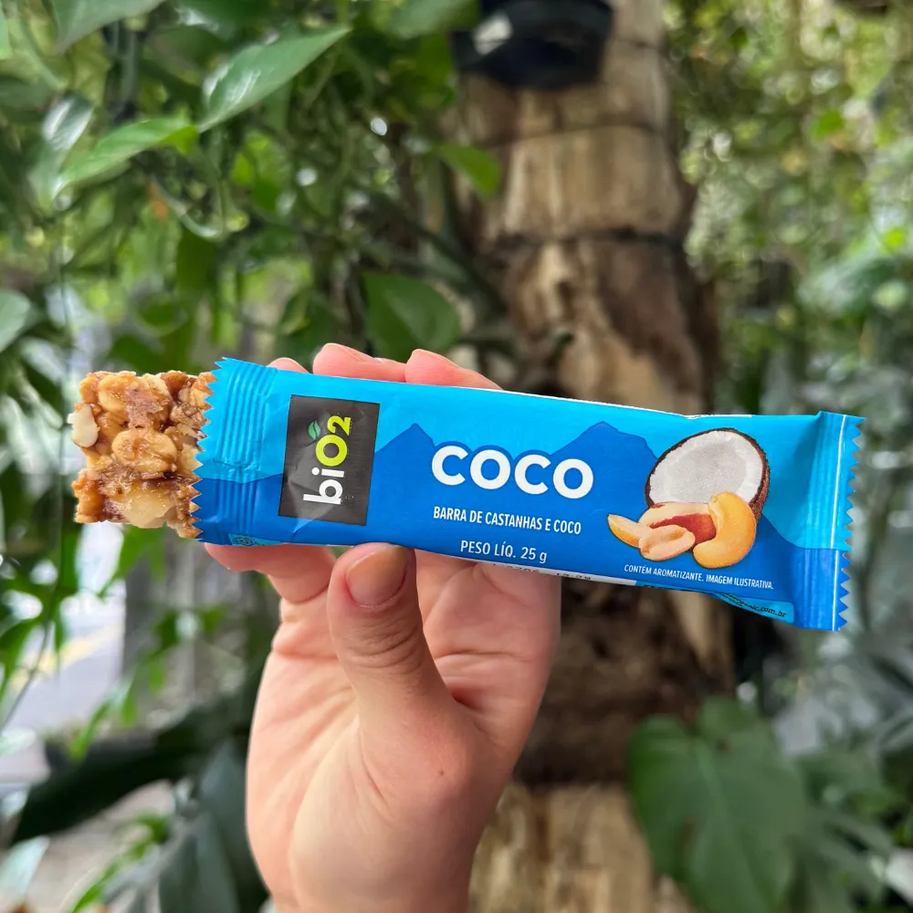 Parte da barra de Castanhas e Frutas biO2, vegana e sem glúetn, sabor Coco, para fora da embalagem de 25 gramas, exibindo a textura das castanhas e do coco.