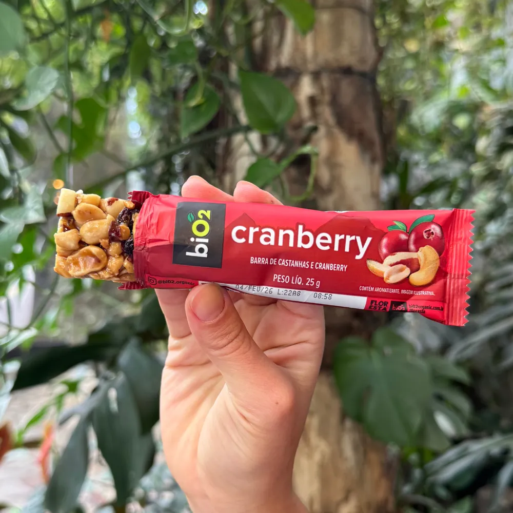 Parte da barra de Castanhas e Frutas biO2, vegana e sem glúetn, sabor Cranberry, para fora da embalagem de 25 gramas, exibindo a textura das castanhas e do cranberry.