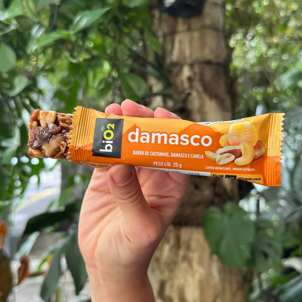 Parte da barra de Castanhas e Frutas biO2, vegana e sem glúetn, sabor Damasco, para fora da embalagem de 25 gramas, exibindo a textura das castanhas e do damasco.