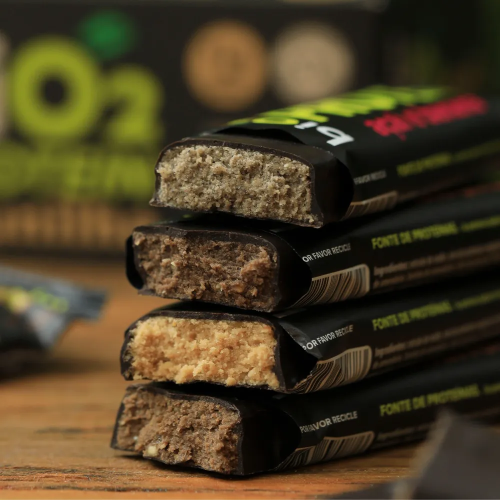 Pilha de pedaços de Barras de Proteína biO2, veganas e sem glúten, mostrando o corte e os quatro sabores, em tábua de madeira.