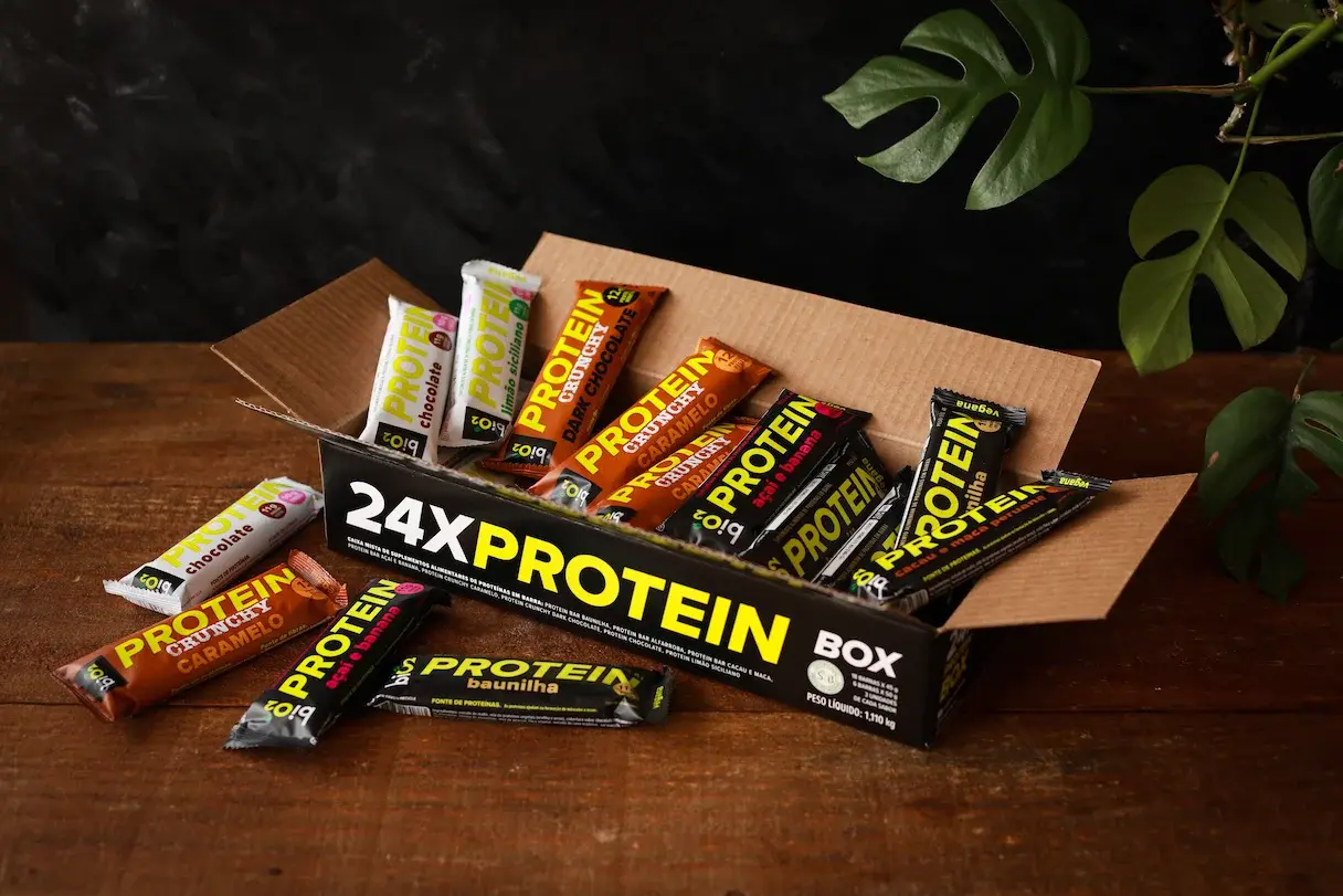 biO2 Protein Box em uma mesa de madeira com uma planta costela de adão ao fundo
