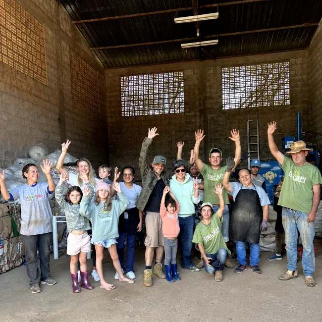 Diversas pessoas da com a mão pro alto dentro de um galpão de reciclagem em Piranguçu - MG do coletivo União dos Catadores de Piranguçu