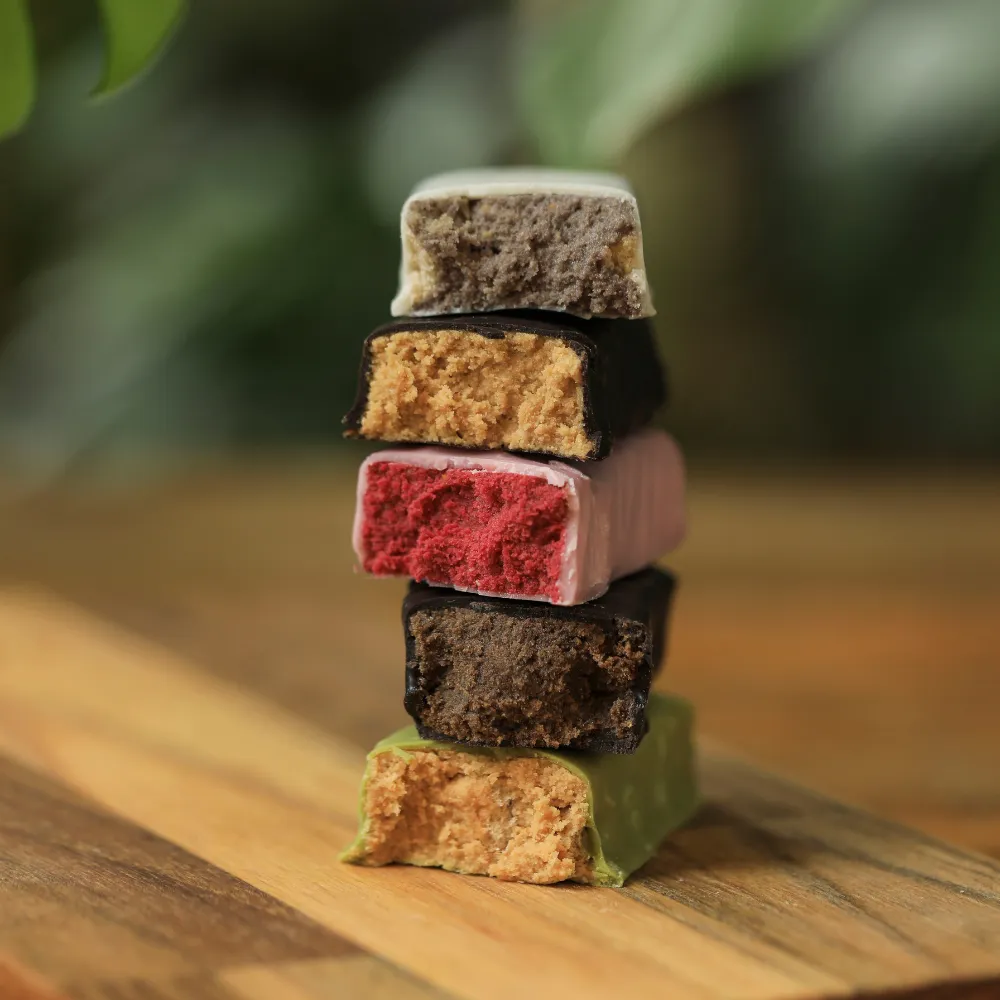 Pilha de pedaços de Barras de Proteína Crocante biO2, veganas e sem glúten, mostrando o corte e os diferentes sabores, em tábua de madeira.