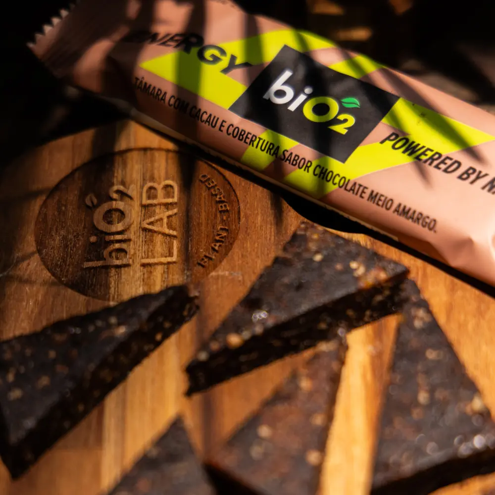 Energy Bar de Tâmara com Cacau e cobertura de chocolate meio amargo, cortada em pedaços sobre uma tábua de madeira com o logo biO2 LAB.